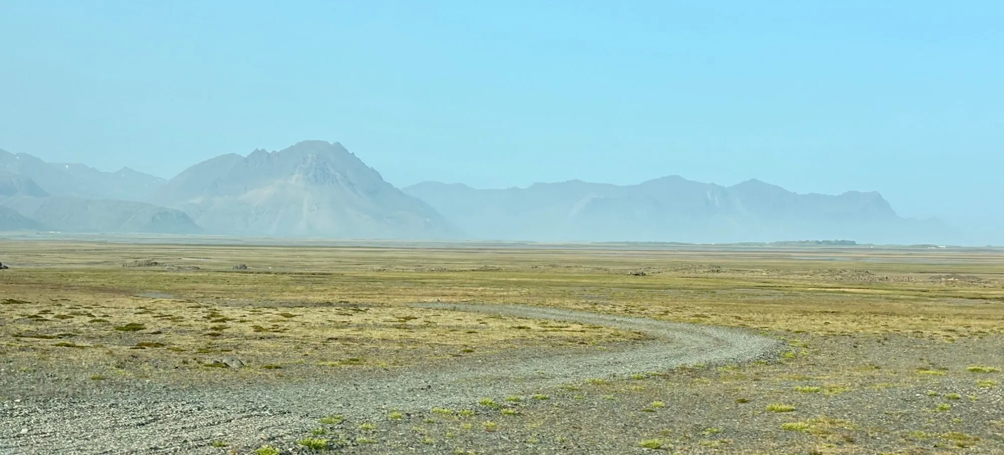 Weite Landschaft mit Weg vor einer Bergkette